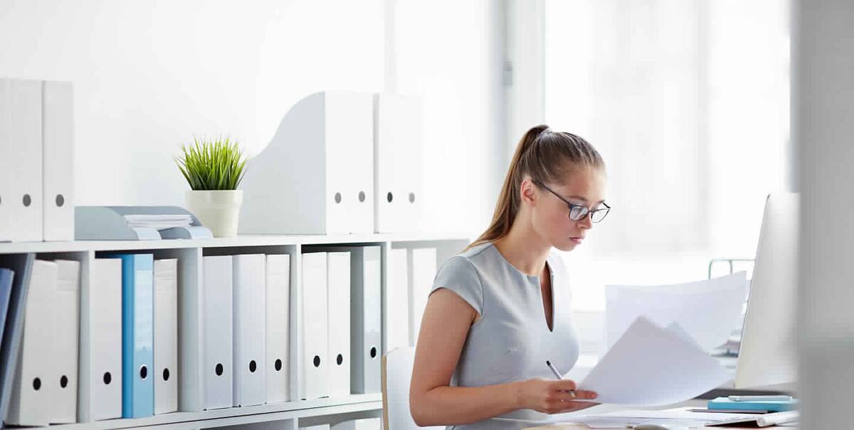 Bookkeeper working through paperwork in a bright office lined with folders